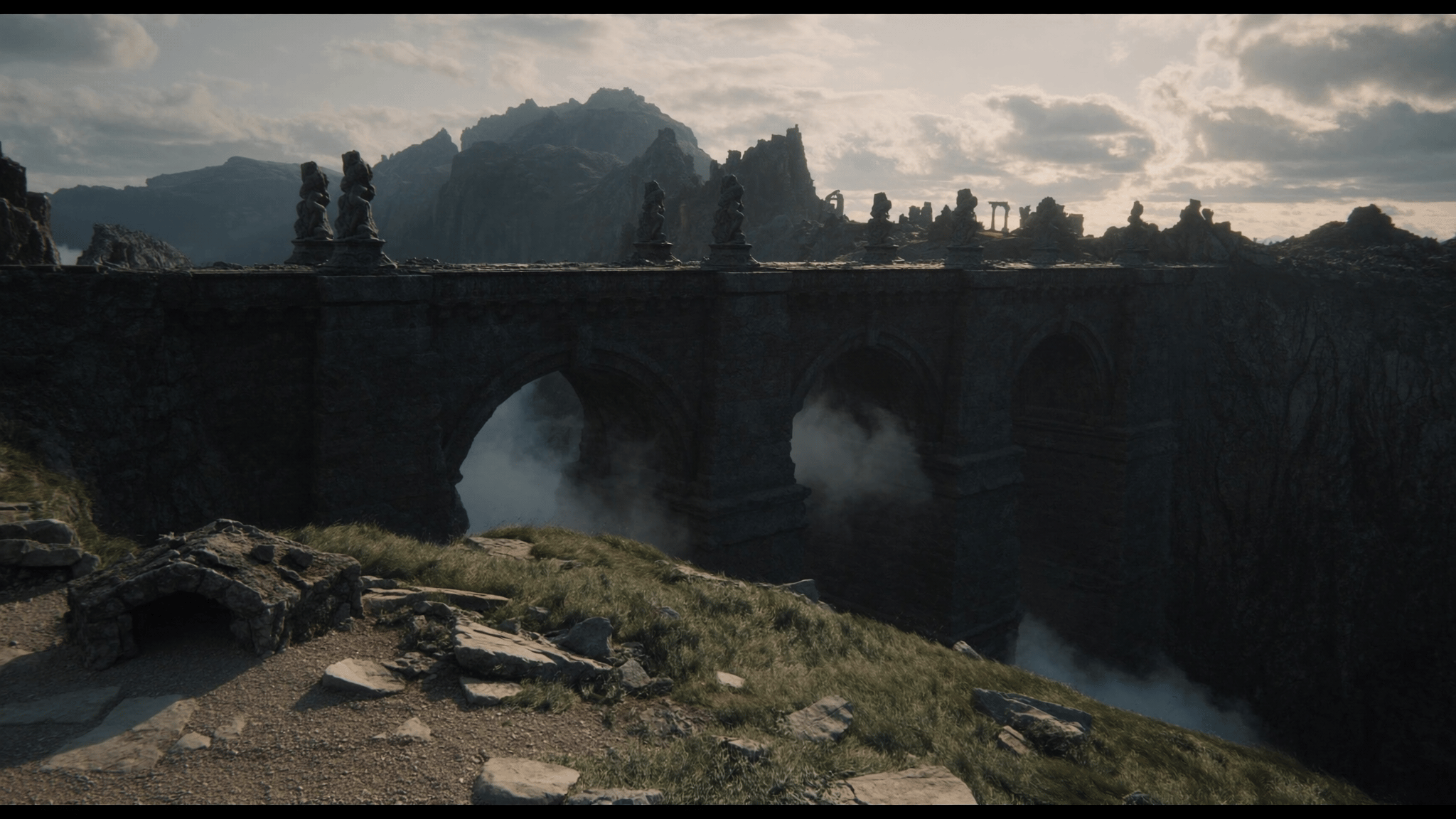 A colossal weathered stone bridge with tall arches spanning a mist-filled ravine between rocky cliffs
